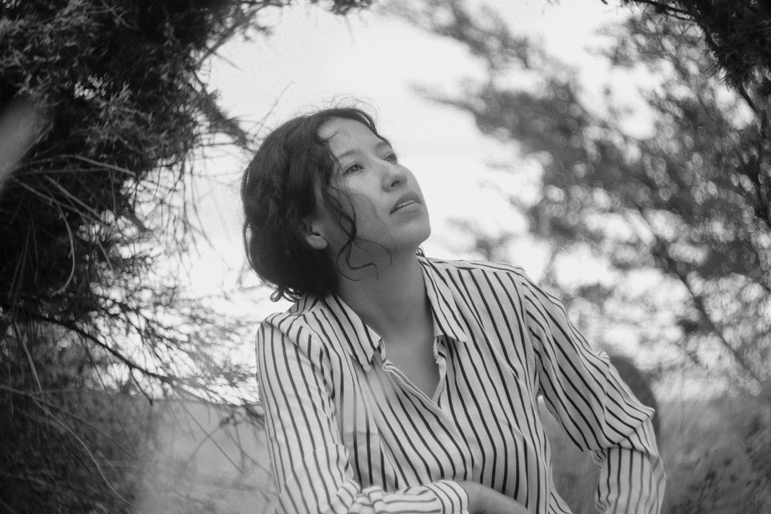 Retrato en blanco y negro de Sasha Salaverry sentada bajo ramas de árboles.