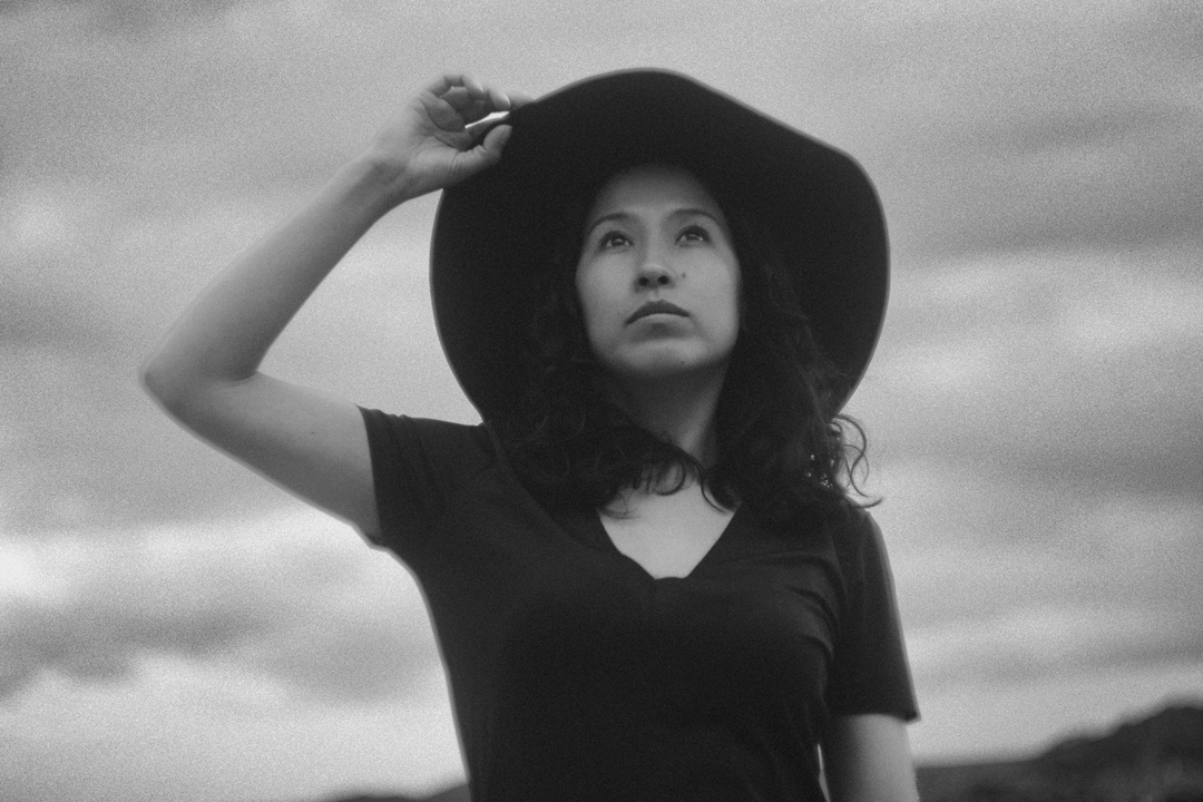 Retrato en blanco y negro de Sasha Salaverry ajustándose un sombrero de ala ancha.