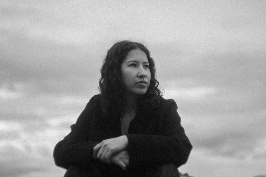 Retrato sentado en blanco y negro de Sasha Salaverry ante un paisaje abierto.