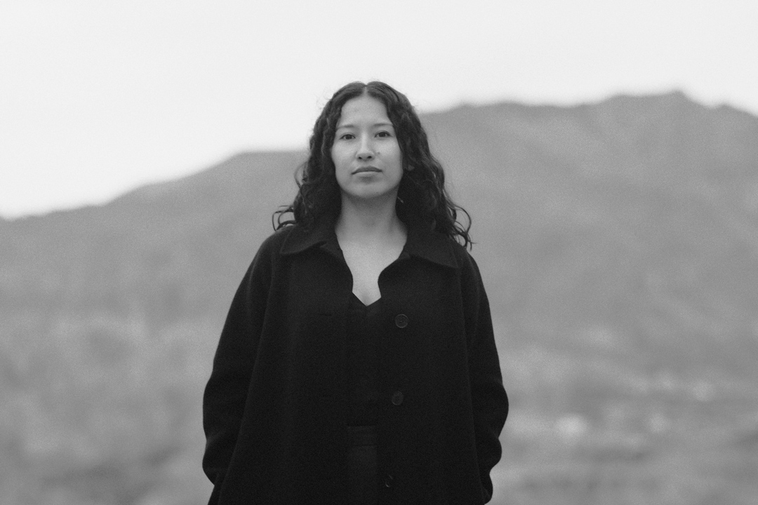 Retrato en blanco y negro de la actriz boliviana Sasha Salaverry de pie ante montañas.